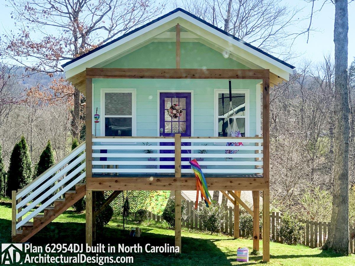 House plan exterior: One-story cottage with a covered front porch, white railing, pitched gable roof, and purple-accented front door.
