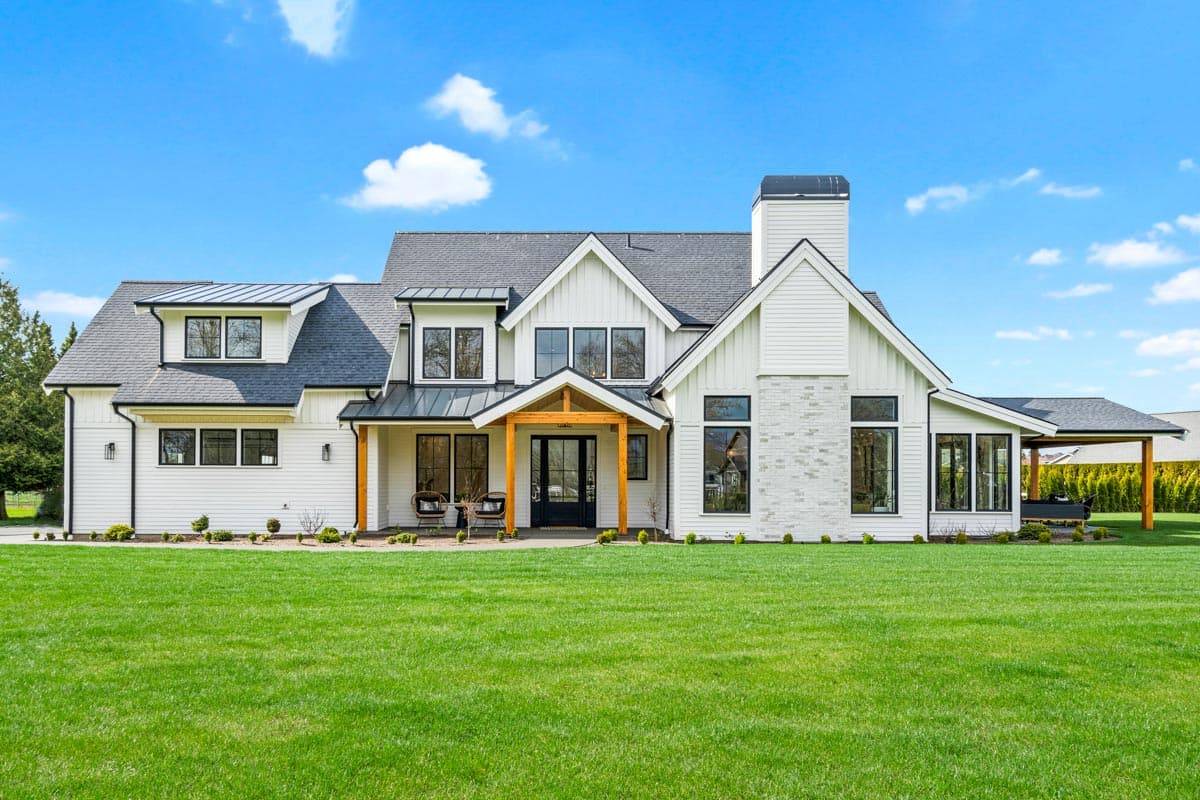 House plan exterior. Two-story Modern Farmhouse with gabled roof, covered porch, and exposed rafter tails. Features a stone-clad chimney and dormers.