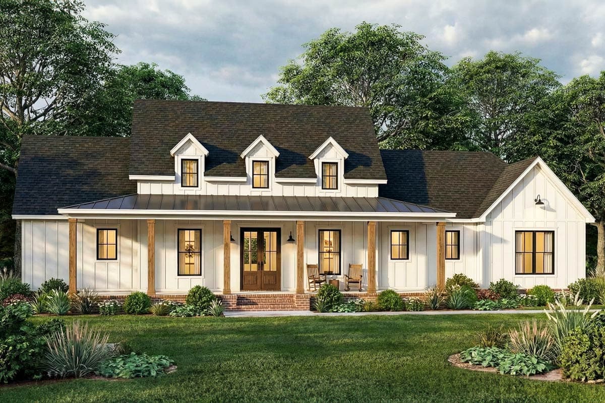 A white farmhouse with a large front porch and dark trim. Features include three dormer windows, a brick landing, and lush green landscaping.