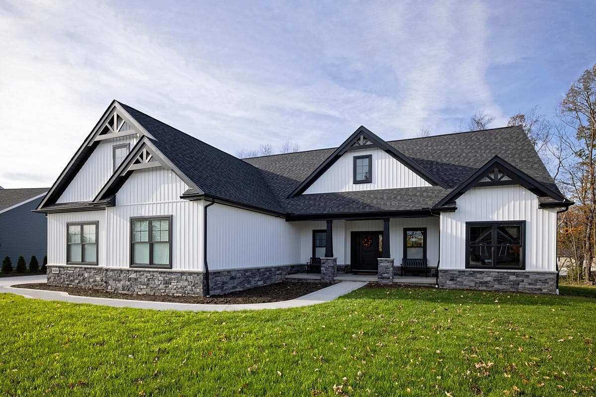 Modern Farmhouse style house plan exterior with white board and batten siding, stone foundation, gables with decorative trusses, and covered porch.