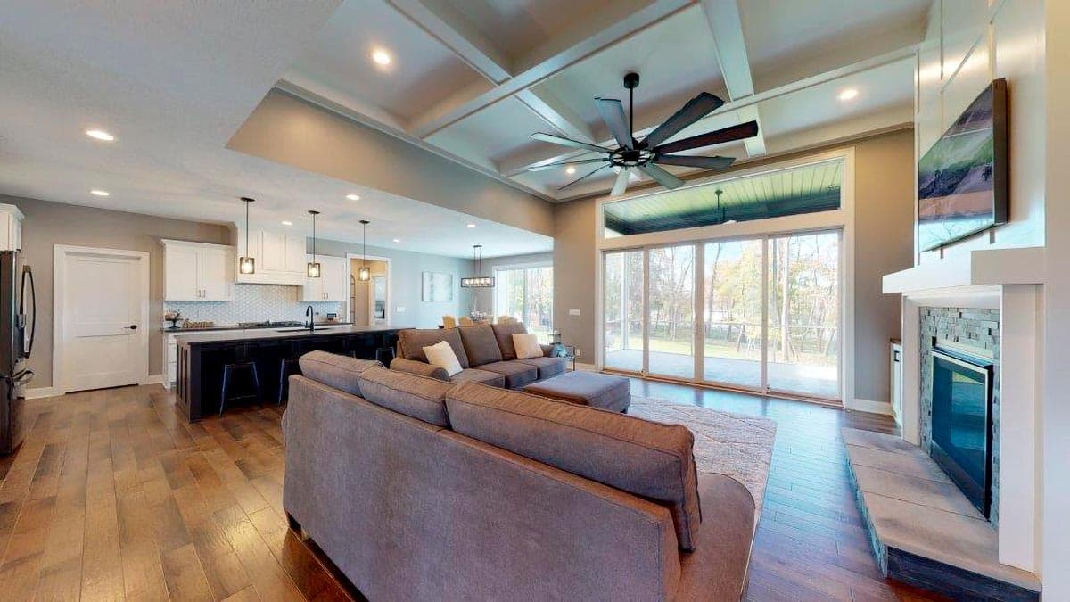 Open concept great room with coffered ceiling, large fan, fireplace, and expansive windows.