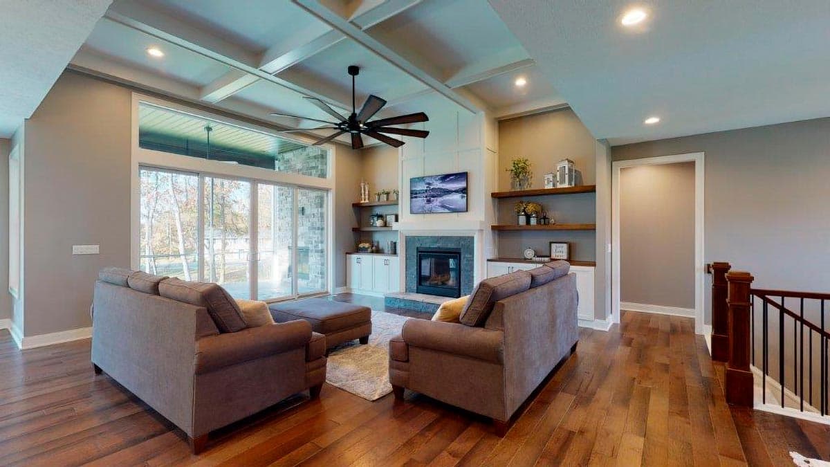 Living room with coffered ceiling, fireplace, built-ins, large windows, and a ceiling fan.
