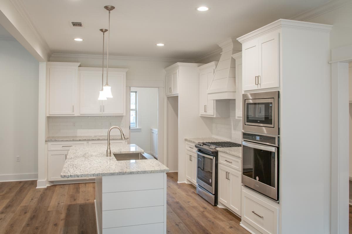 Contemporary kitchen featuring an island with sink, white cabinetry, subway tile backsplash, stainless steel appliances, and pendant lights.