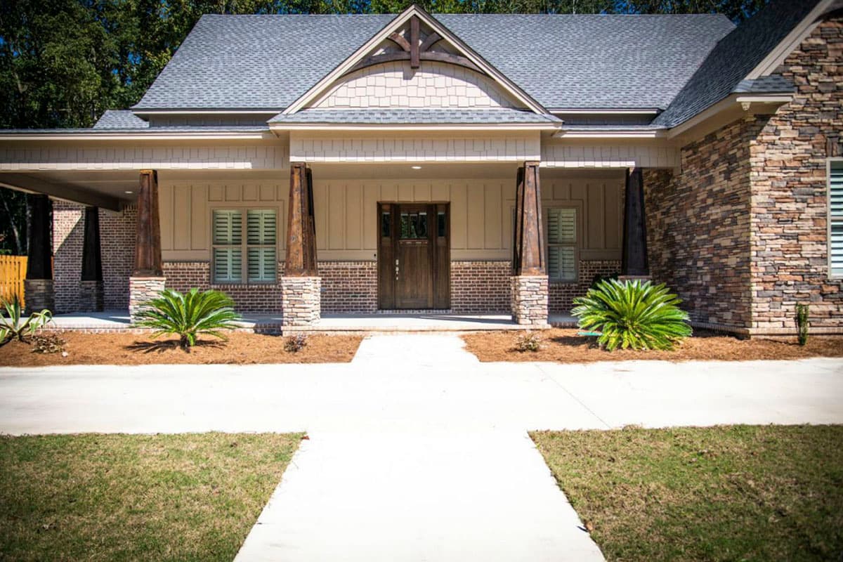 House plan exterior: one-story home with covered entry, stone accents, wood columns, and gabled dormer.