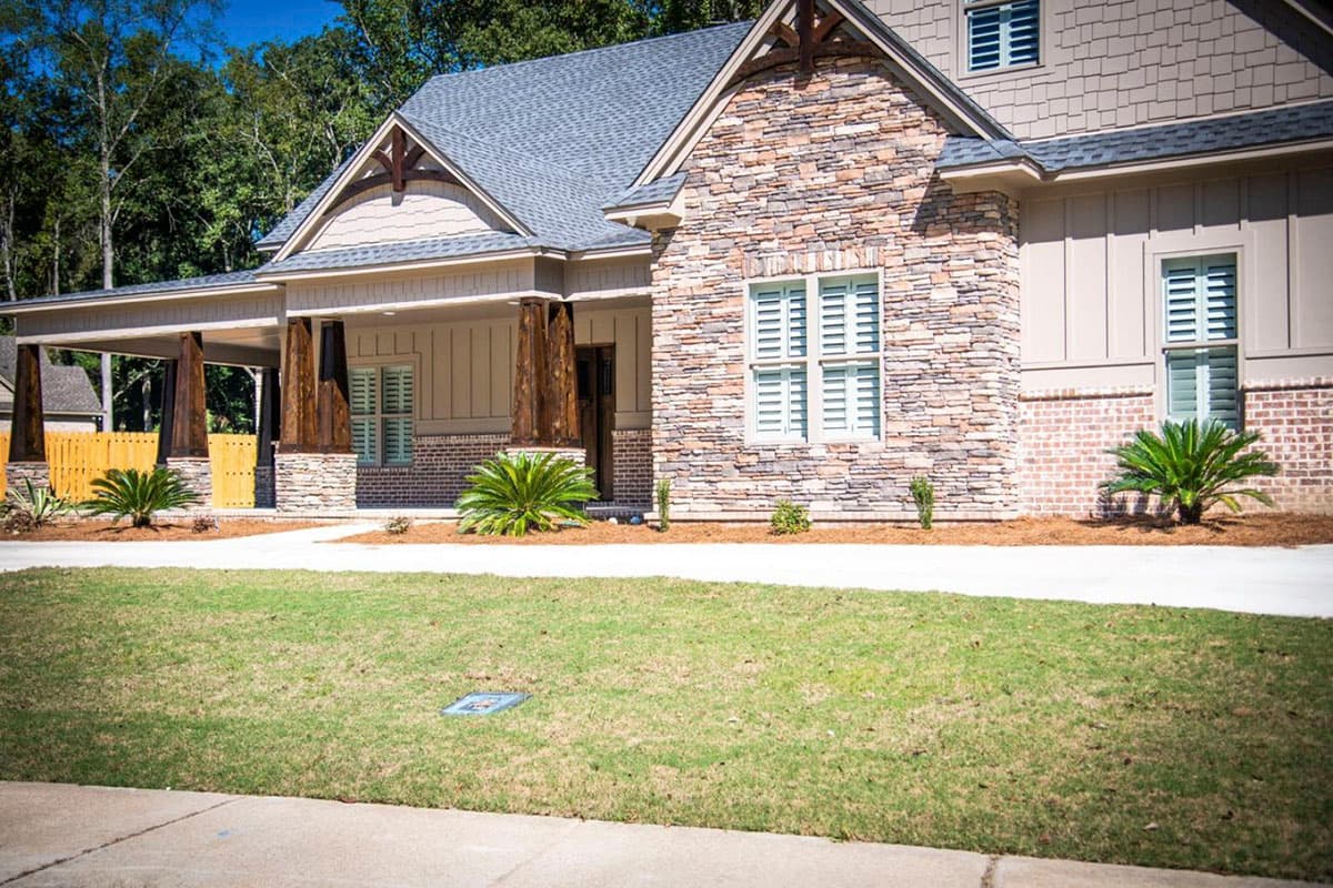 House plan exterior featuring stacked stone, brick, vertical siding, gabled dormers, and covered porch with wooden columns.