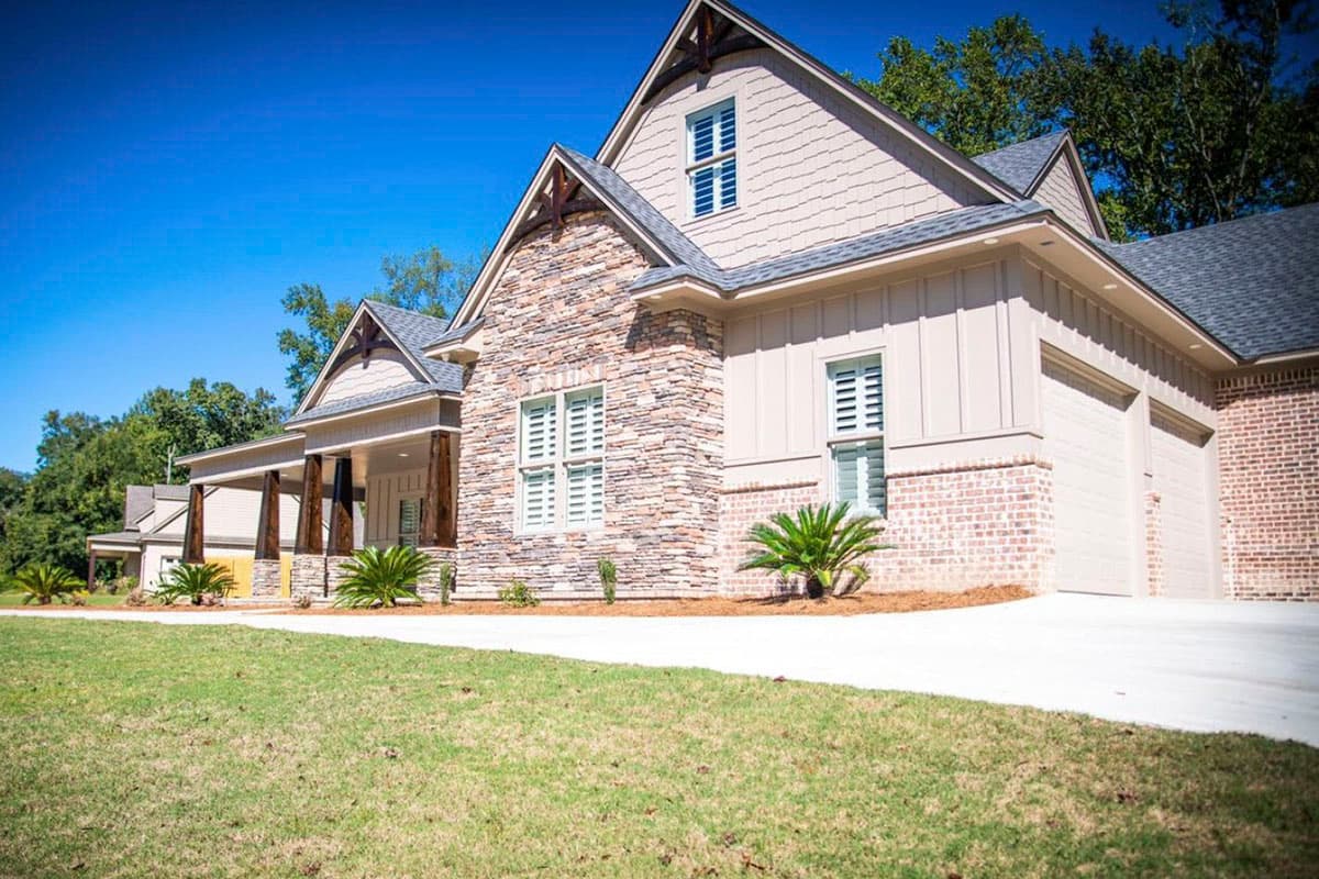 House plan exterior with stone and vinyl siding, covered porch, gabled dormer, and attached three-car garage.