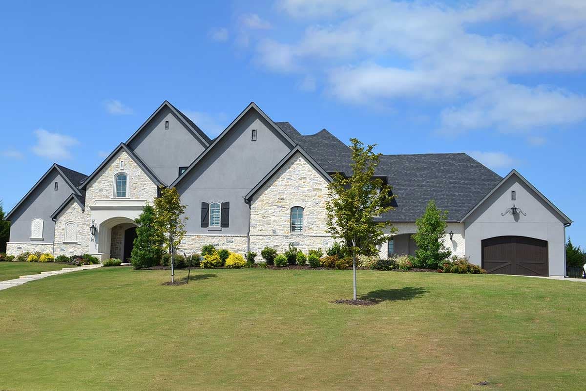 House plan exterior. Two-story, European-style home with gabled roof, arched entry, stone and stucco exterior, and attached garage.