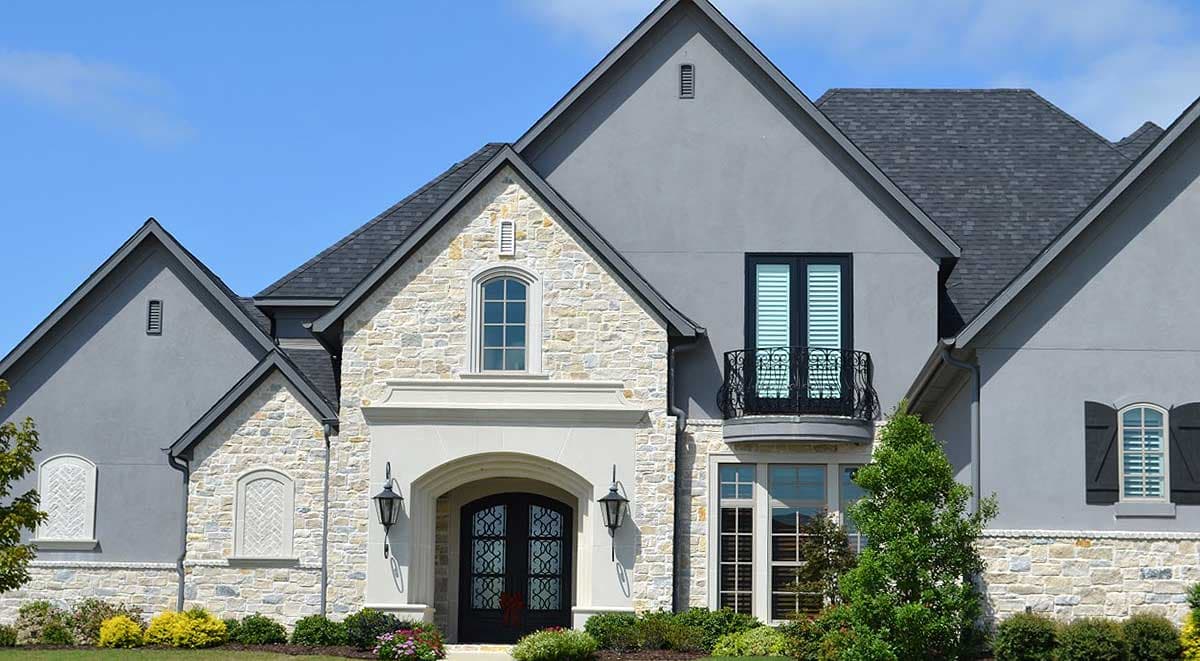 House plan exterior featuring stone and stucco facade, arched entryway with double doors, and a second-story Juliet balcony.