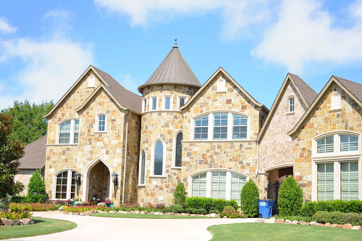 House plan exterior with stone facade, turrets, gabled roofs, arched entry, and multiple large windows.