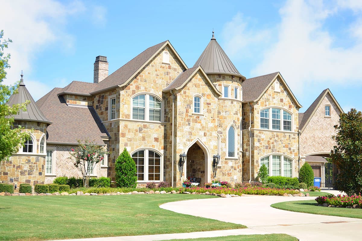 House plan exterior with two stories. Stone facade, arched entry, multiple gables, and turret roof. Includes a driveway and manicured lawn.