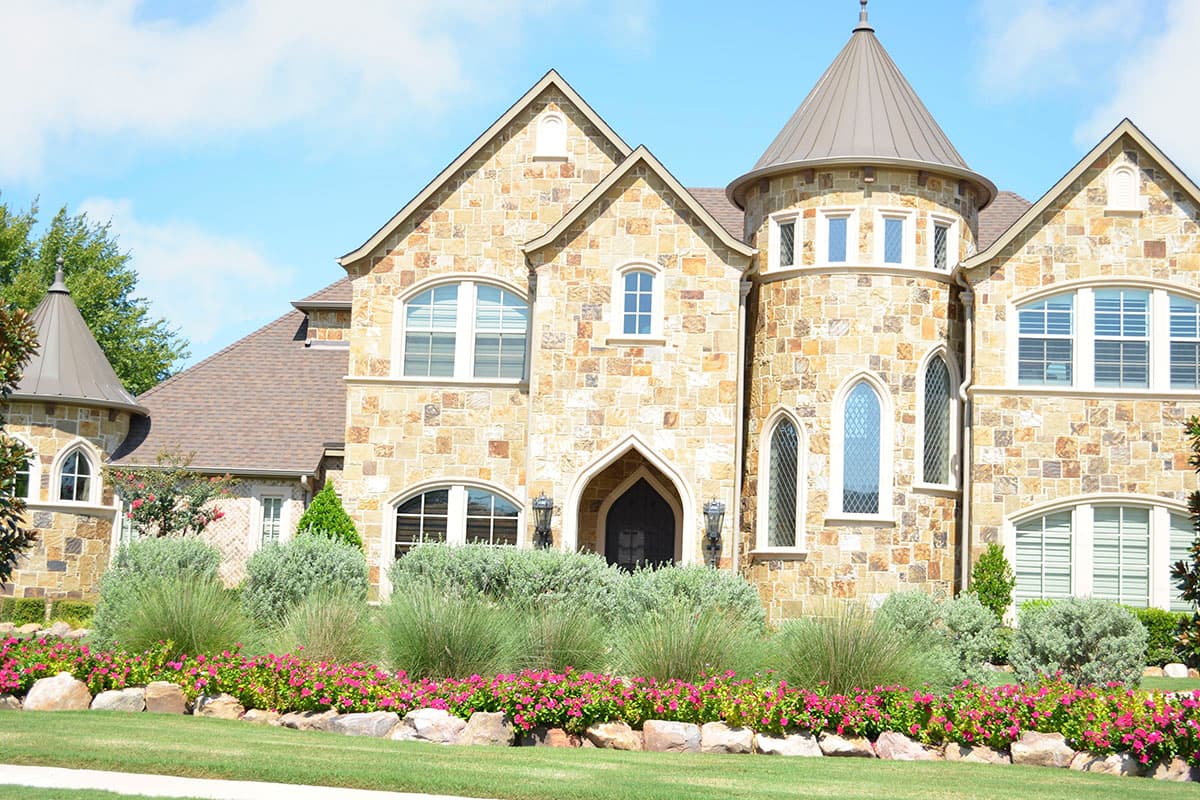 House plan exterior with stone facade, gables, arched windows, and conical turrets.
