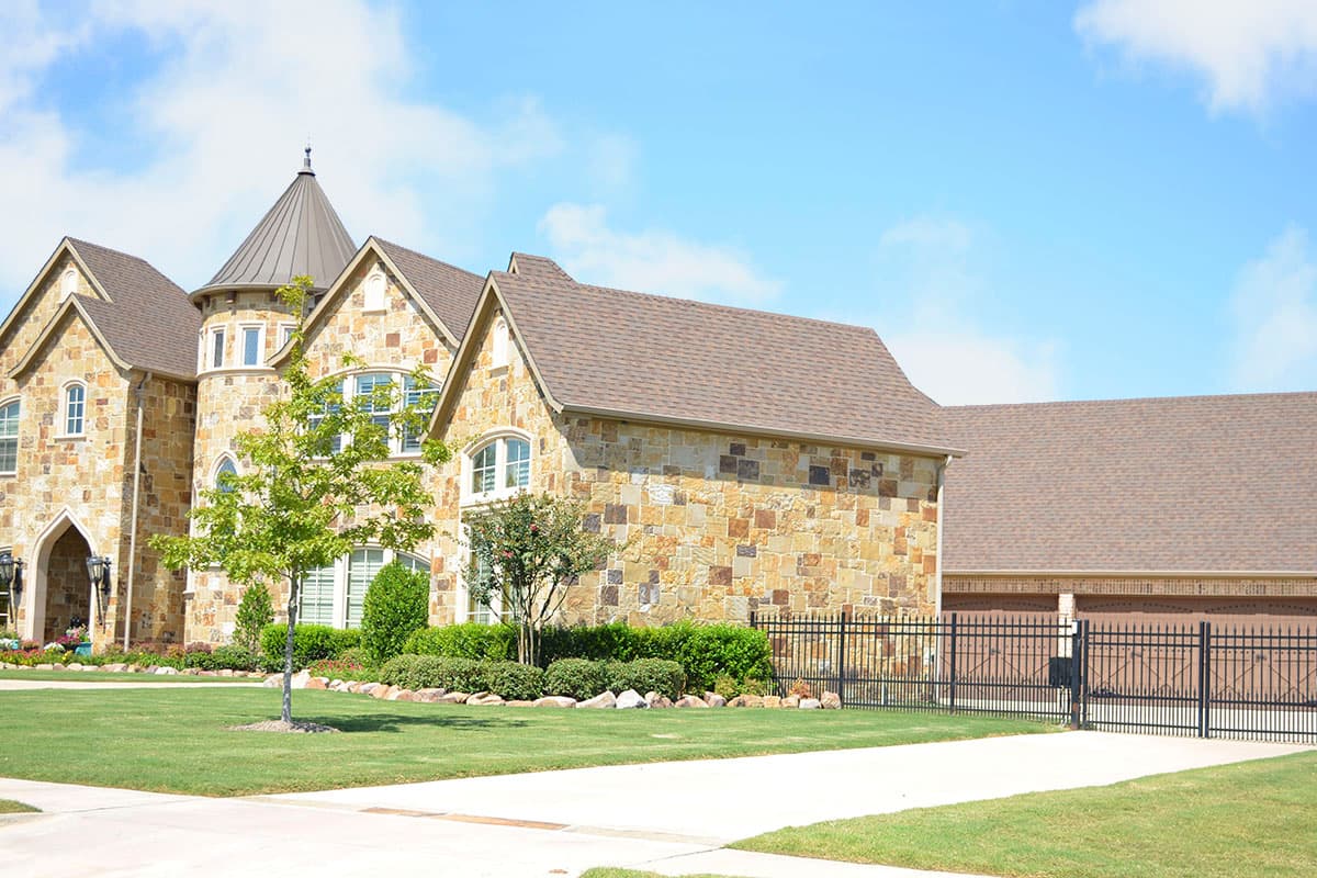 House plan exterior featuring stone facade, multiple gables, conical turret, and attached three-car garage.