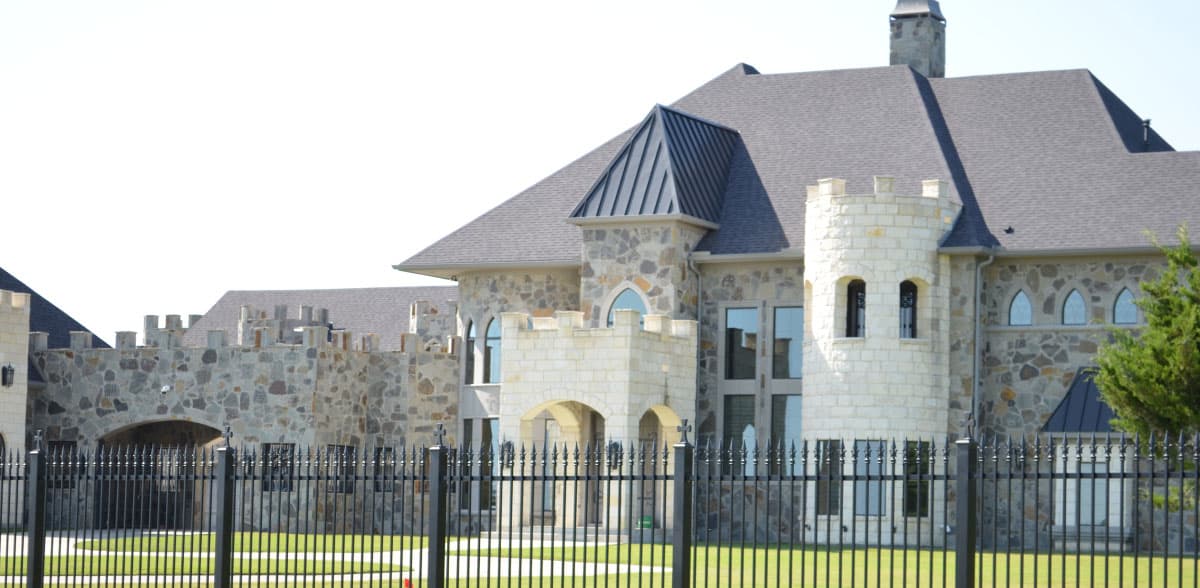 House plan exterior with stone facade, crenellated parapets, arched entryways, and prominent tower.