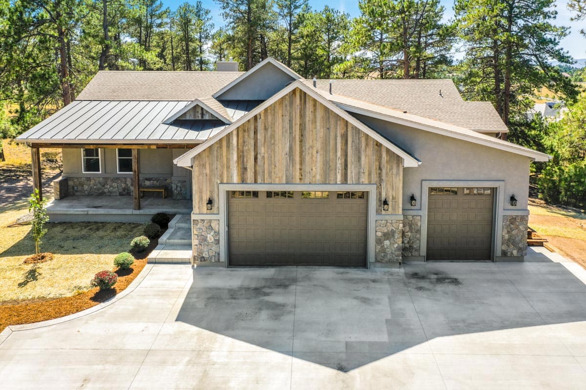 House plan exterior: Single-story home with metal roof, covered porch, stone accents, wood siding, and a triple-car garage.