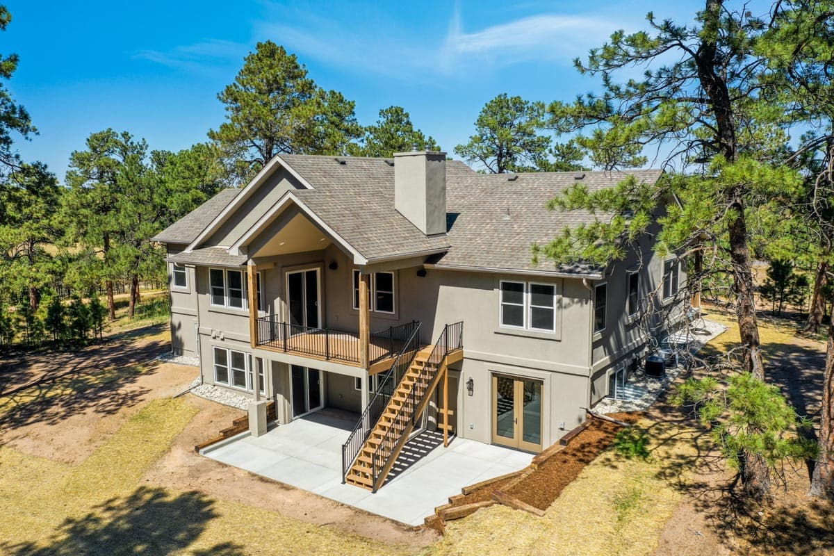 House plan exterior of a two-story home with a covered upper deck, exterior staircase, and prominent chimney.