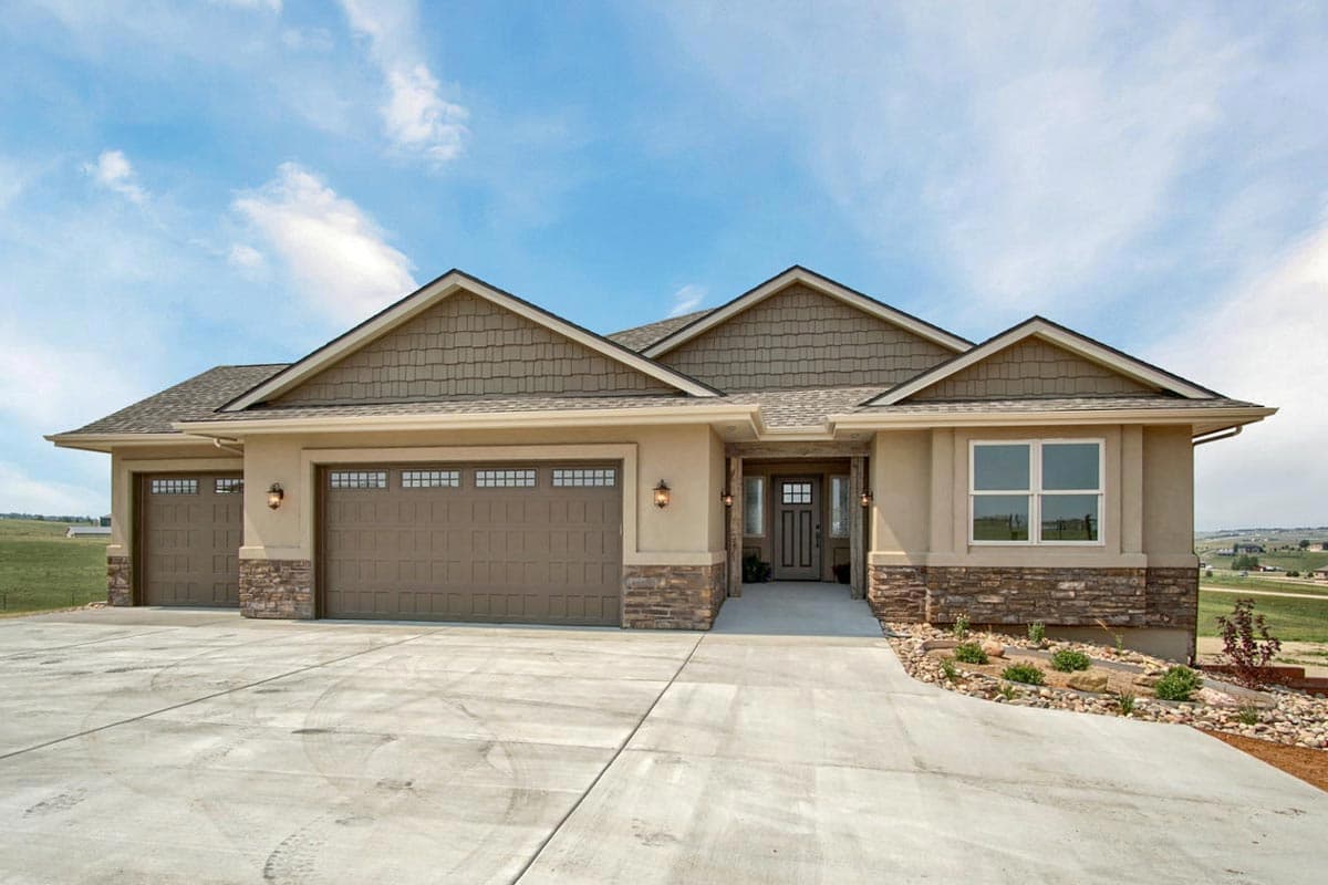 House plan exterior. Ranch style with a two-car garage, gabled roof, and stone accents. The entry features a covered porch.