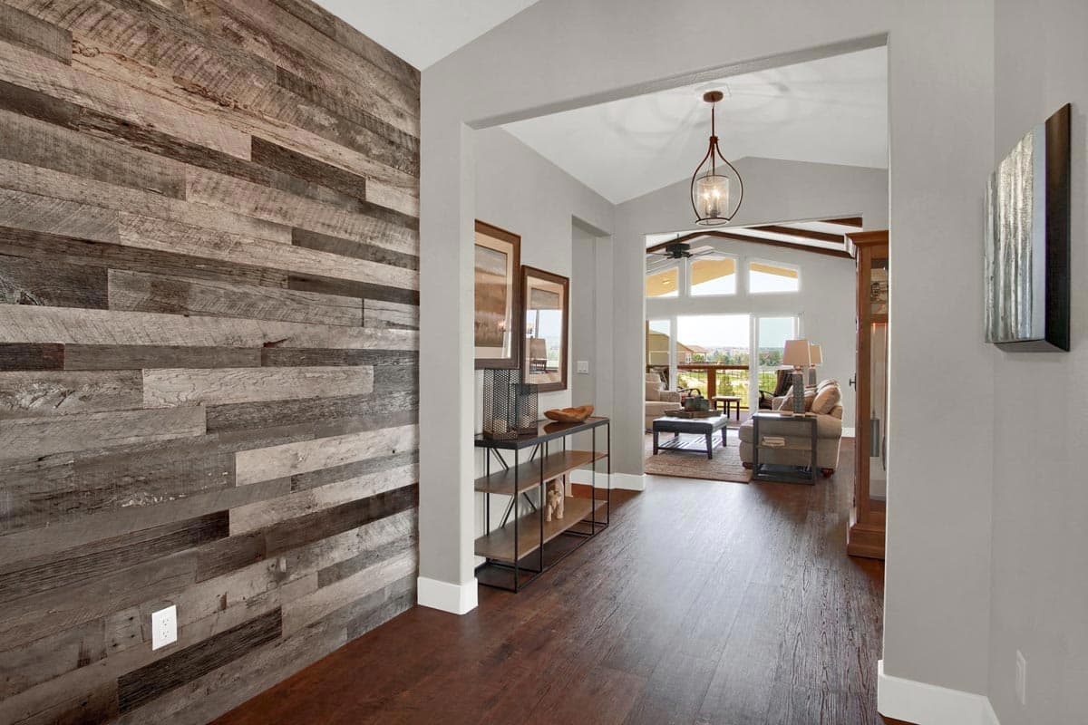 Interior view of a house with a distressed wood accent wall, console table, and a living room with vaulted ceiling and large windows.