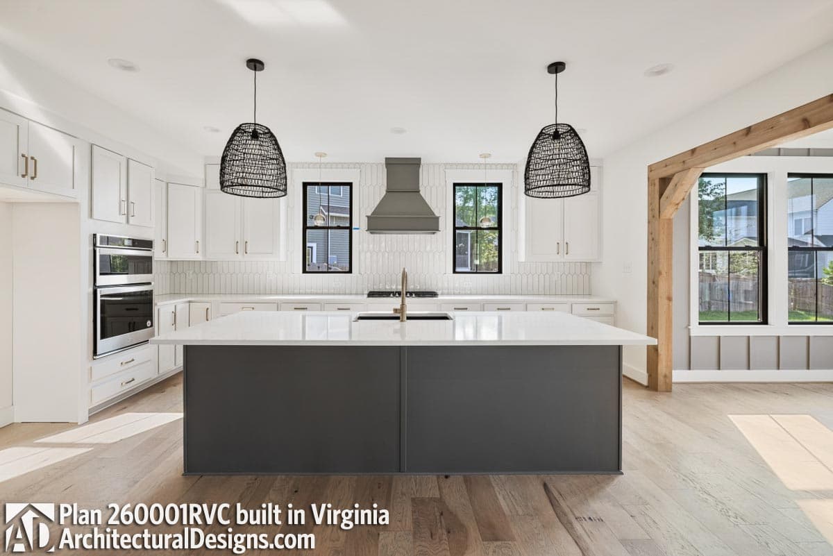 Kitchen interior with dark gray island, white cabinetry, stainless steel appliances, and decorative pendant lights.