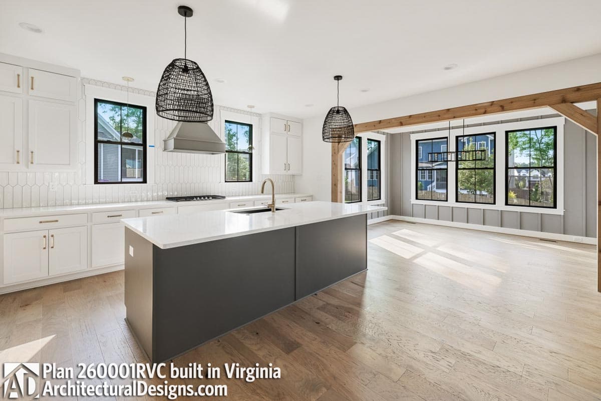 Kitchen and great room with large island, white cabinets, stainless steel range hood, and wooden beams.