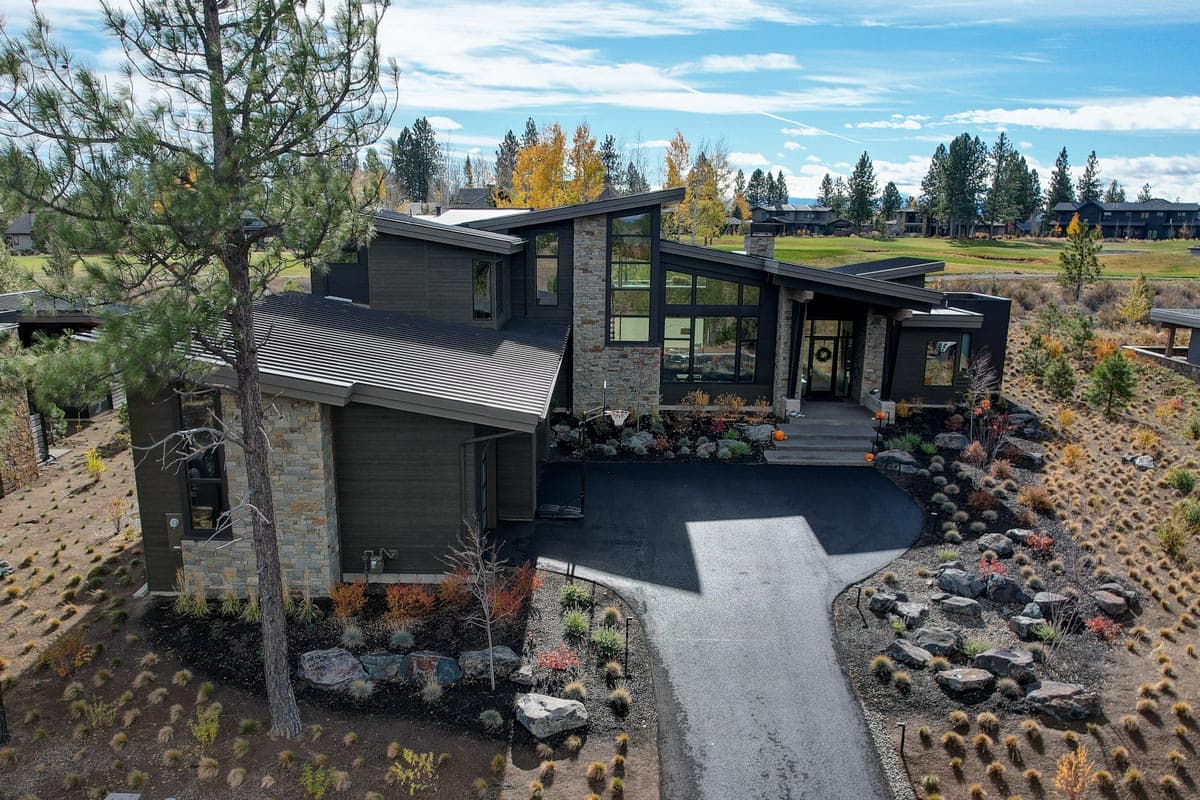 Modern house plan exterior with stone accents, dark siding, large windows, and a sloping metal roof.