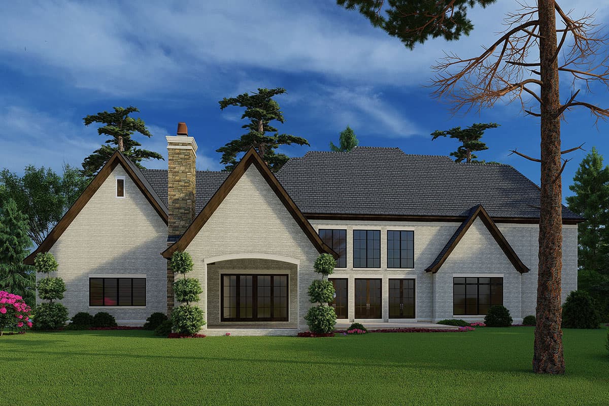 House plan exterior showing a multi-story home with gables, a prominent stone chimney, arched entry, and large grid windows.