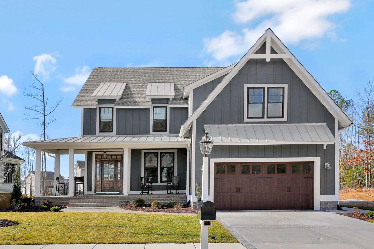 Modern Farmhouse house plan exterior: two stories, covered front porch, gabled dormers, and attached two-car garage with wood door.