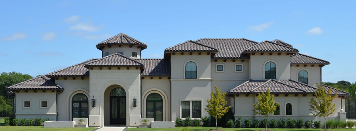 House plan exterior. Two-story Mediterranean-style home with tile roof, arched windows, and a turret. Features include a symmetrical facade.