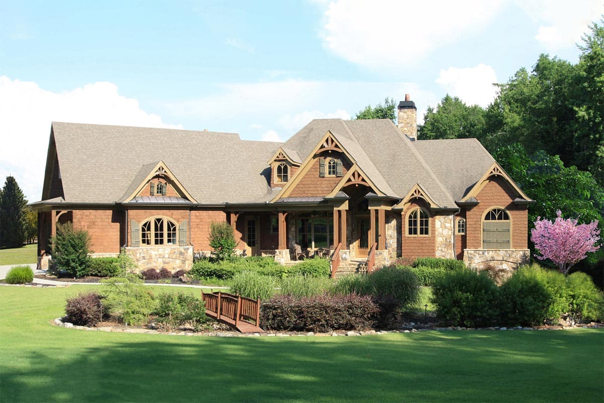House plan exterior. Craftsman style, one-story house with gables, stone accents, and a covered porch. Features include arched windows and a chimney.