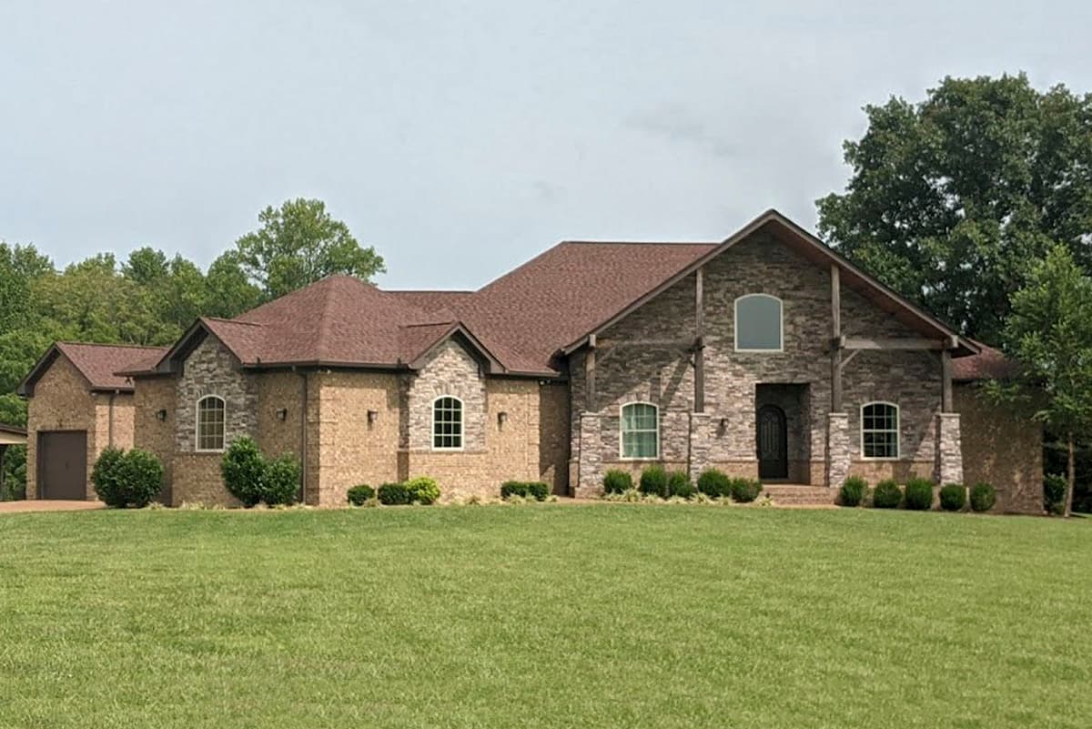 House plan exterior. Two-story home with a brick and stone facade. Features include a gabled roof, arched windows, and a covered entry.