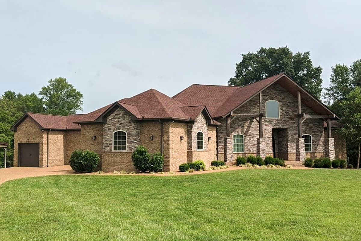 House plan exterior: Two-story home with brick and stone facade, prominent gables, arched windows, and attached two-car garage.