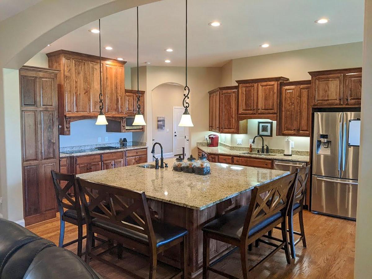 Kitchen featuring a large granite island with pendant lights, dark wood cabinetry, stainless steel refrigerator, and hardwood floors.