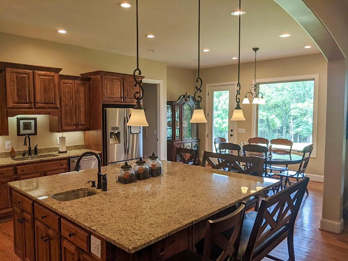 Kitchen with large granite island, dark wood cabinetry, stainless steel appliances, and dining area with large window.