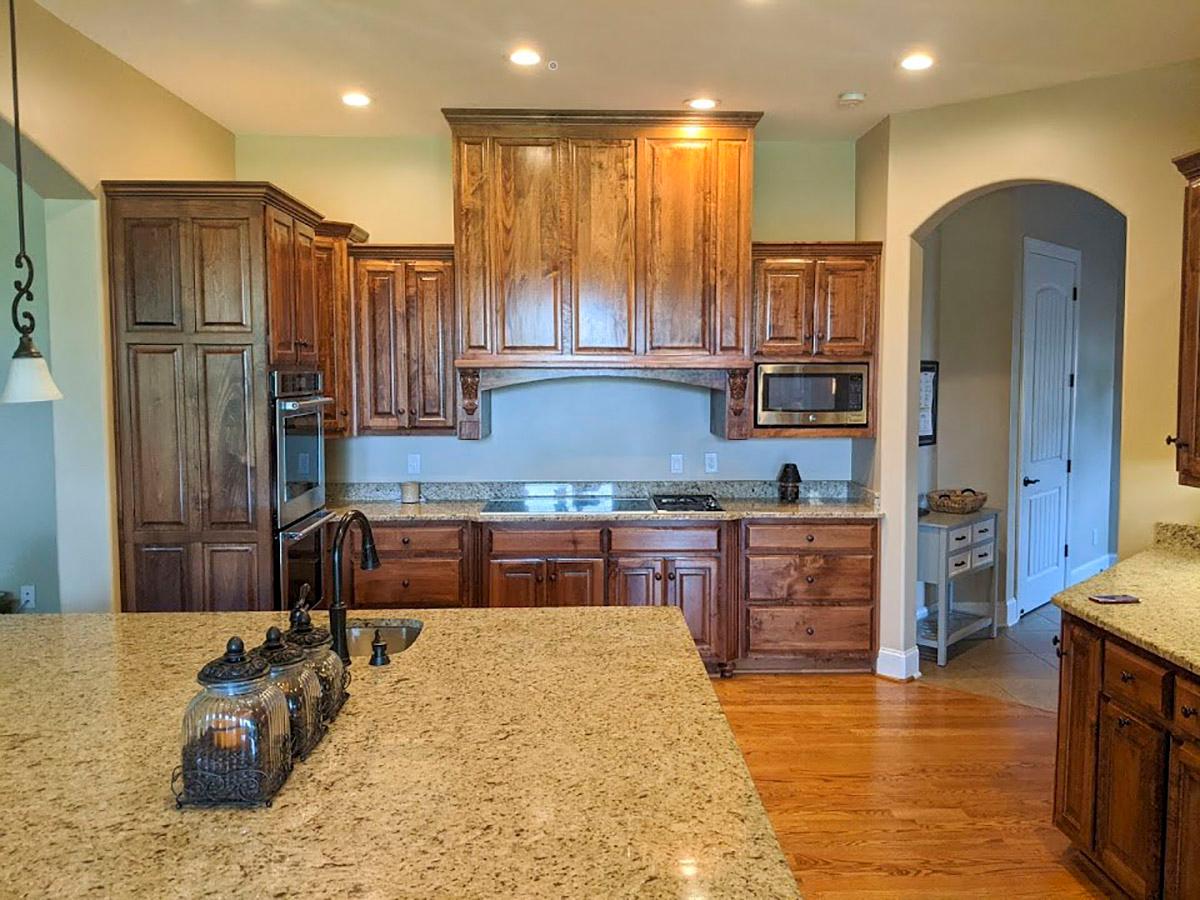 Kitchen with dark wood cabinetry, granite countertops, stainless steel microwave and oven, and a large island.