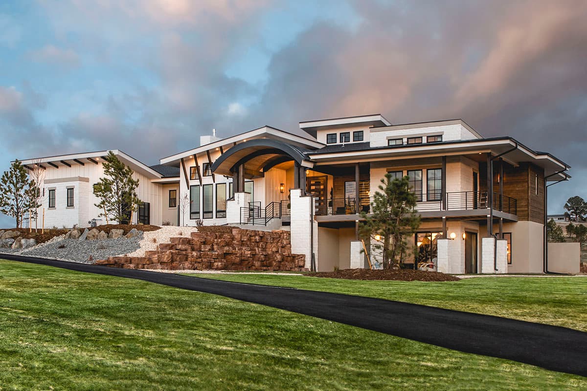 House plan exterior. Two-story modern home with flat and angled rooflines. Features include a curved portico, balcony, and stone accents.