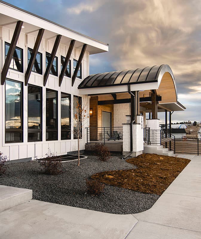 House plan exterior: Modern style with a curved metal roof entry, vertical siding, large windows, and exposed rafter tails.