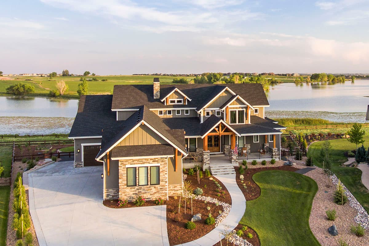 House plan exterior. Modern Farmhouse style, two stories, with a wraparound porch, gables, dormers, and a side-facing garage.