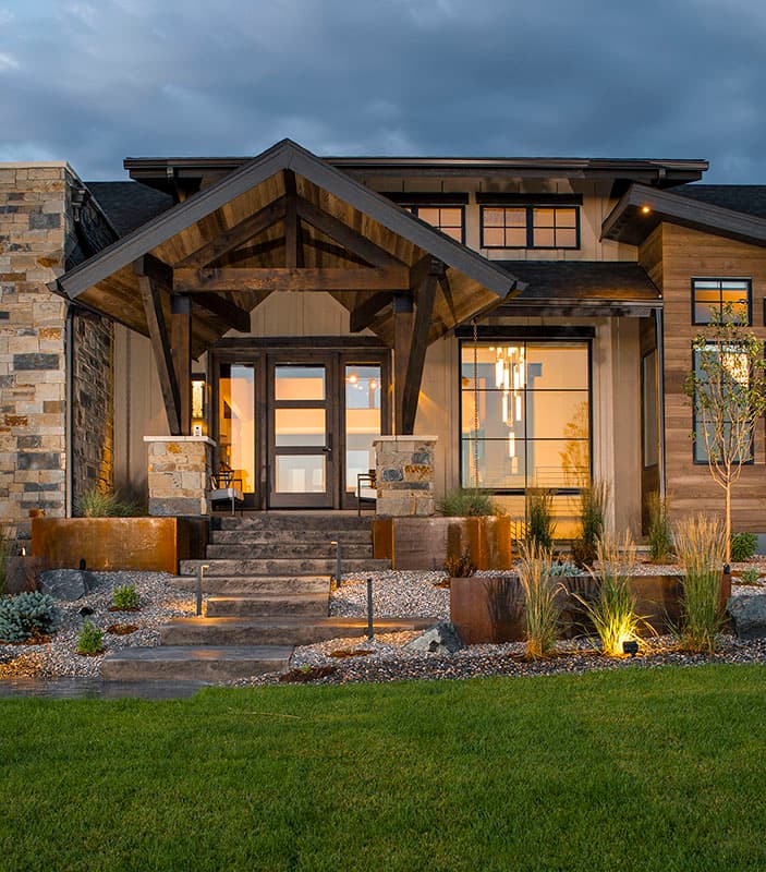 Modern house exterior with stone and wood siding, covered entry with exposed beams, and large windows.