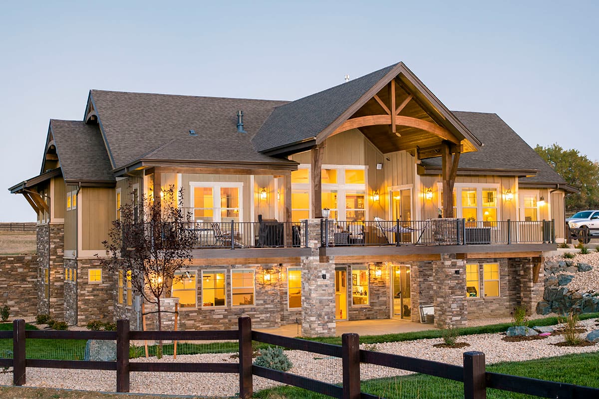 House plan exterior: Modern Farmhouse style, two stories, stone accents, large deck, and exposed wooden beams.