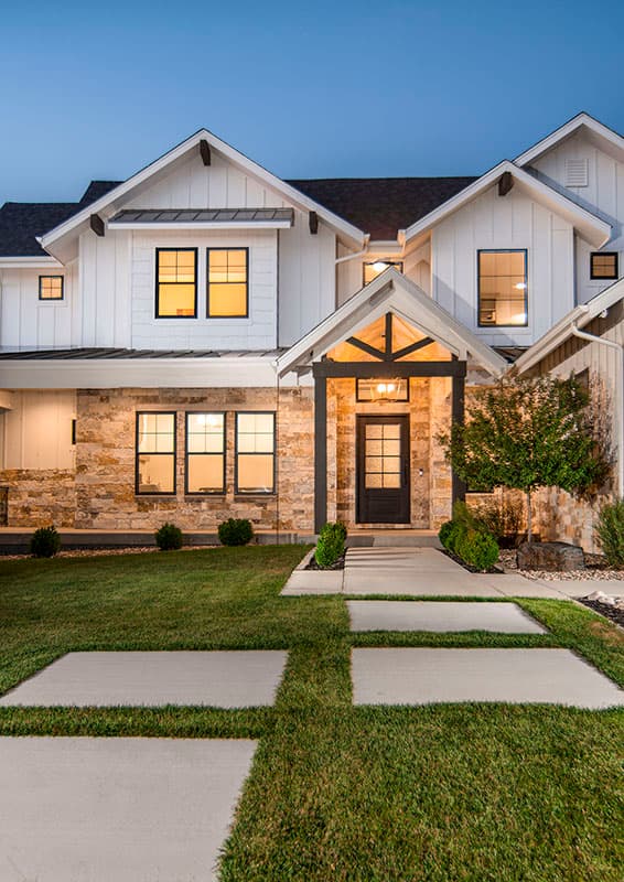 Modern farmhouse exterior with stone and board-and-batten siding, prominent gables, and a covered entry with exposed beams.
