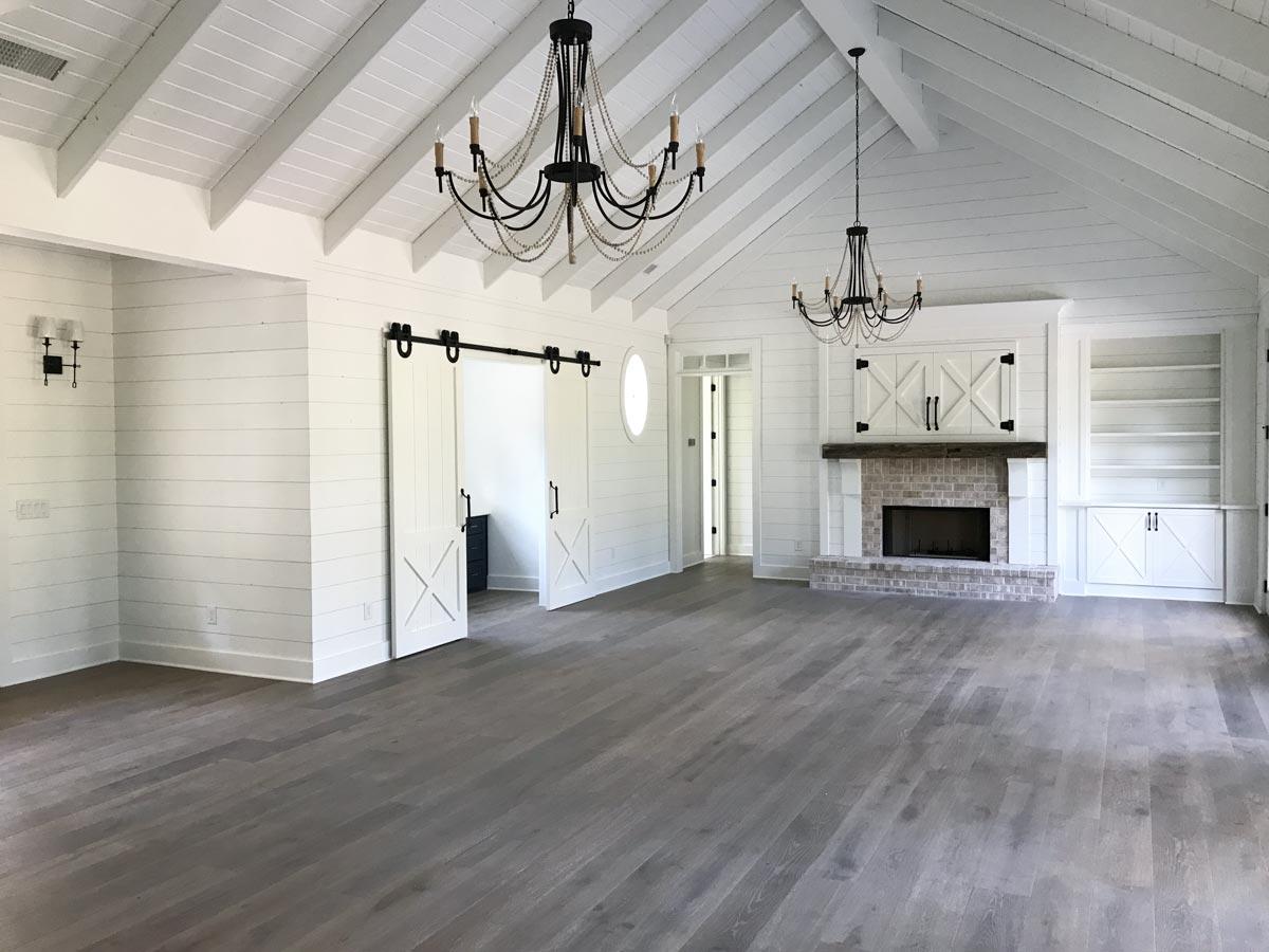Great room with vaulted beamed ceiling, brick fireplace, built-in shelves, and white barn doors.
