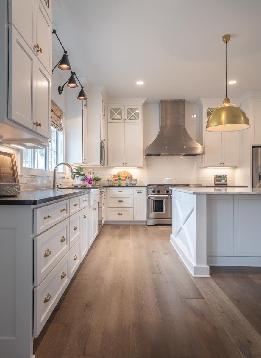 Kitchen with white cabinets, stainless steel range hood, marble-topped island, and pendant lighting.