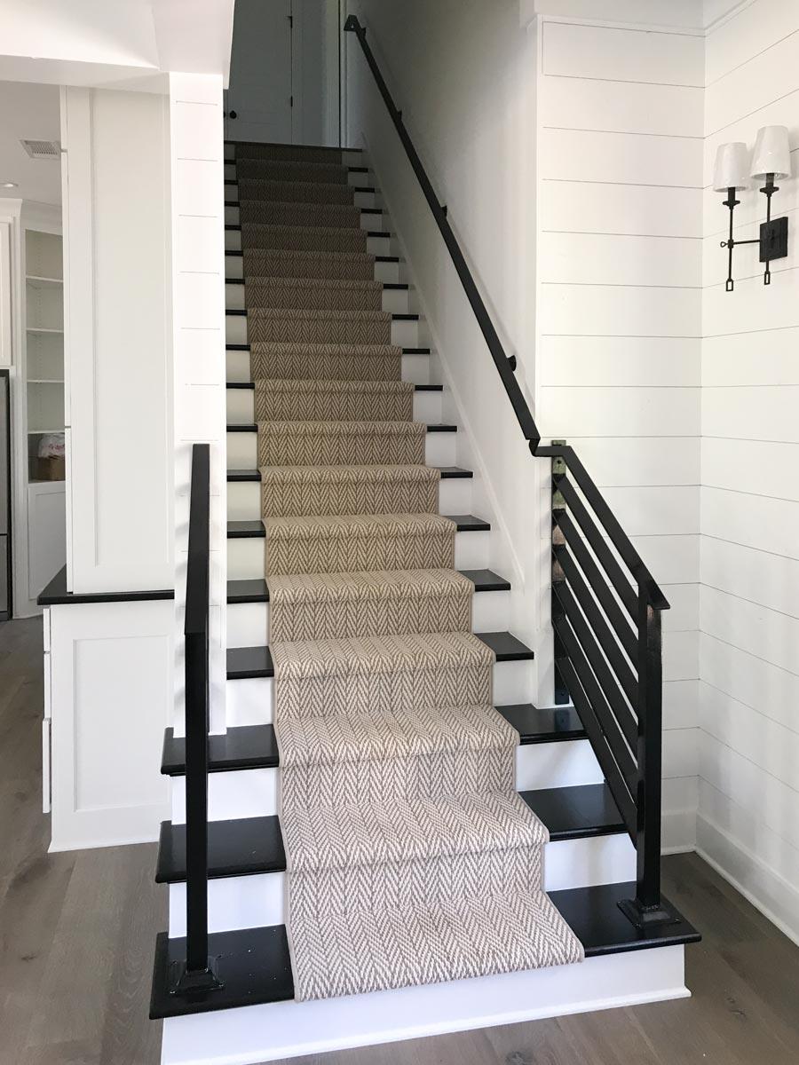 Interior staircase with herringbone patterned runner, black risers and treads, and modern black metal railings.