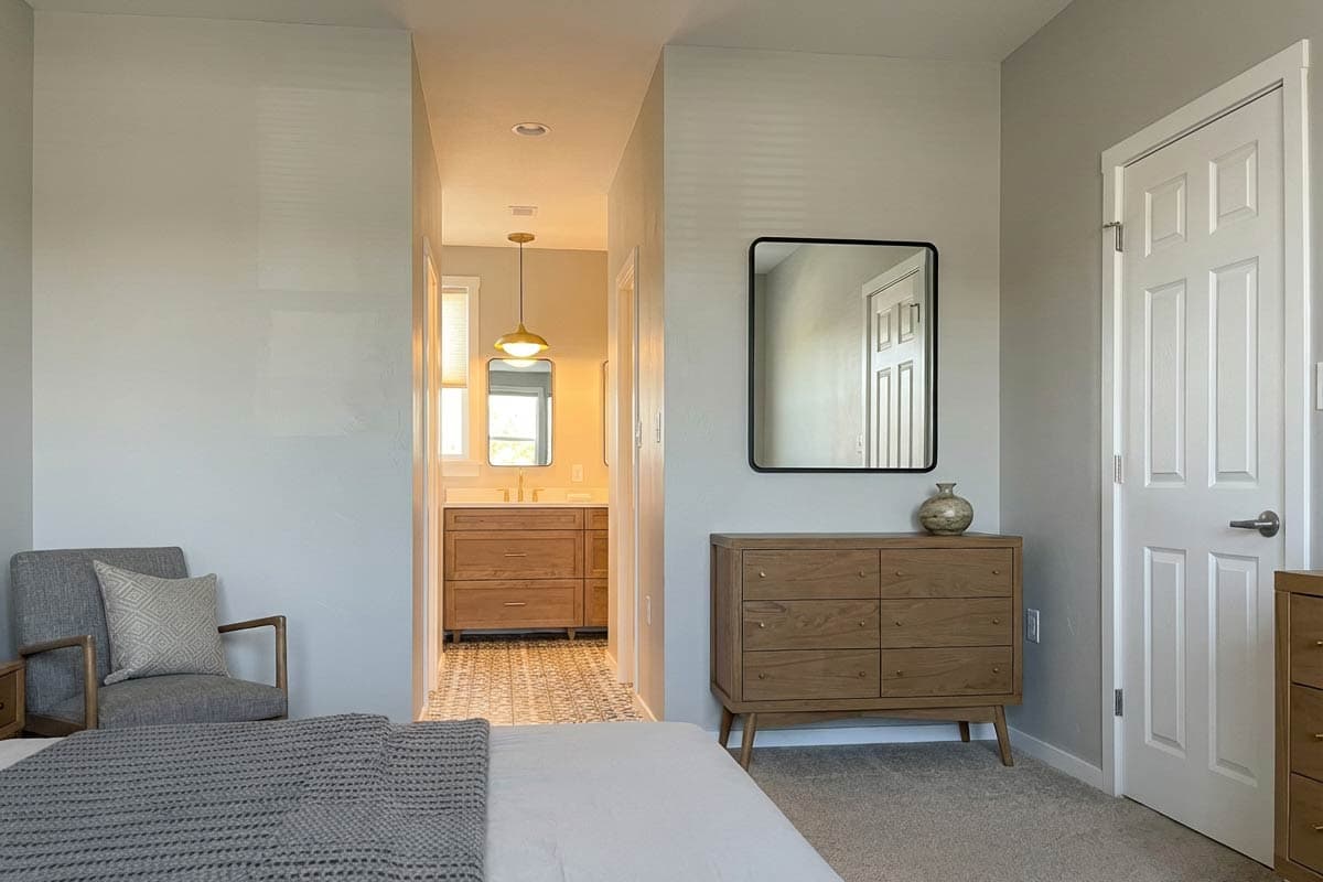 Bedroom and adjacent bathroom with wood vanity and patterned tile floor.