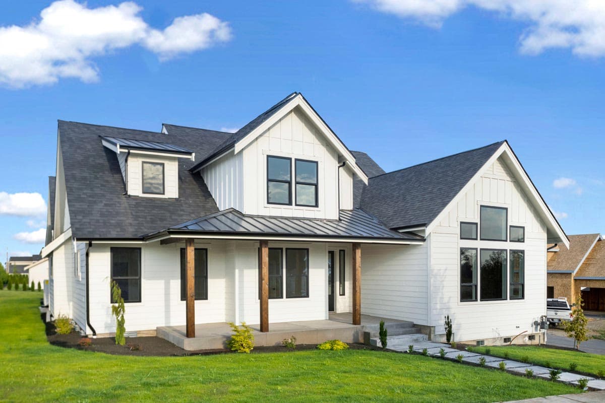 House plan exterior. Modern Farmhouse style, two-story house with a front porch, gables, and dormers. Features dark roof and wood columns.