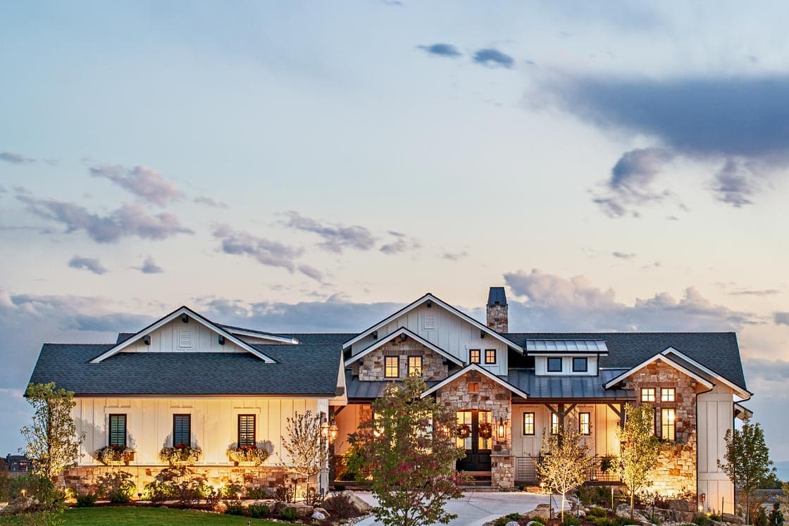 House plan exterior. Modern farmhouse style, one-story. Features include gables, stone accents, a covered porch, and a dark roofline.