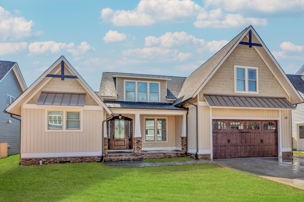 House plan exterior with gables, dormers, covered porch with stone columns, and a two-car garage with wood doors.