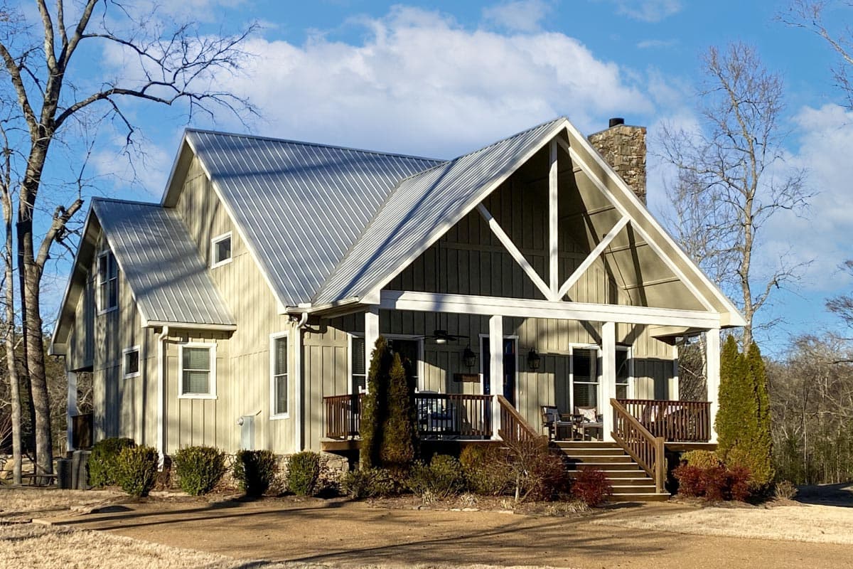 House plan exterior: Modern Farmhouse style, two stories, metal gable roof, stone chimney, and covered front porch with wooden railings.