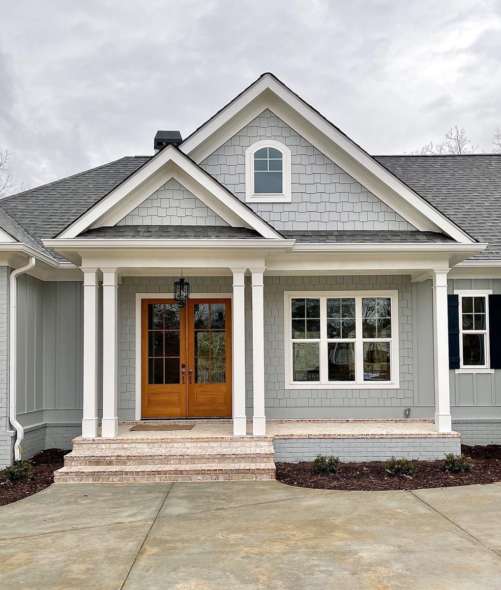 House plan exterior with a gabled roof, arched dormer, and covered porch supported by square columns.