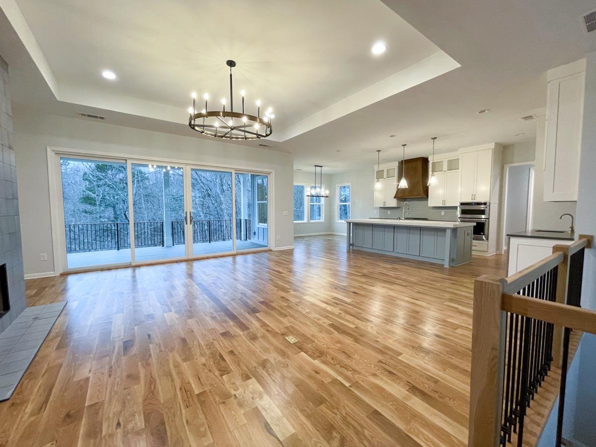 Open concept living space with fireplace, kitchen island, and large sliding doors to deck. Modern chandelier overhead.