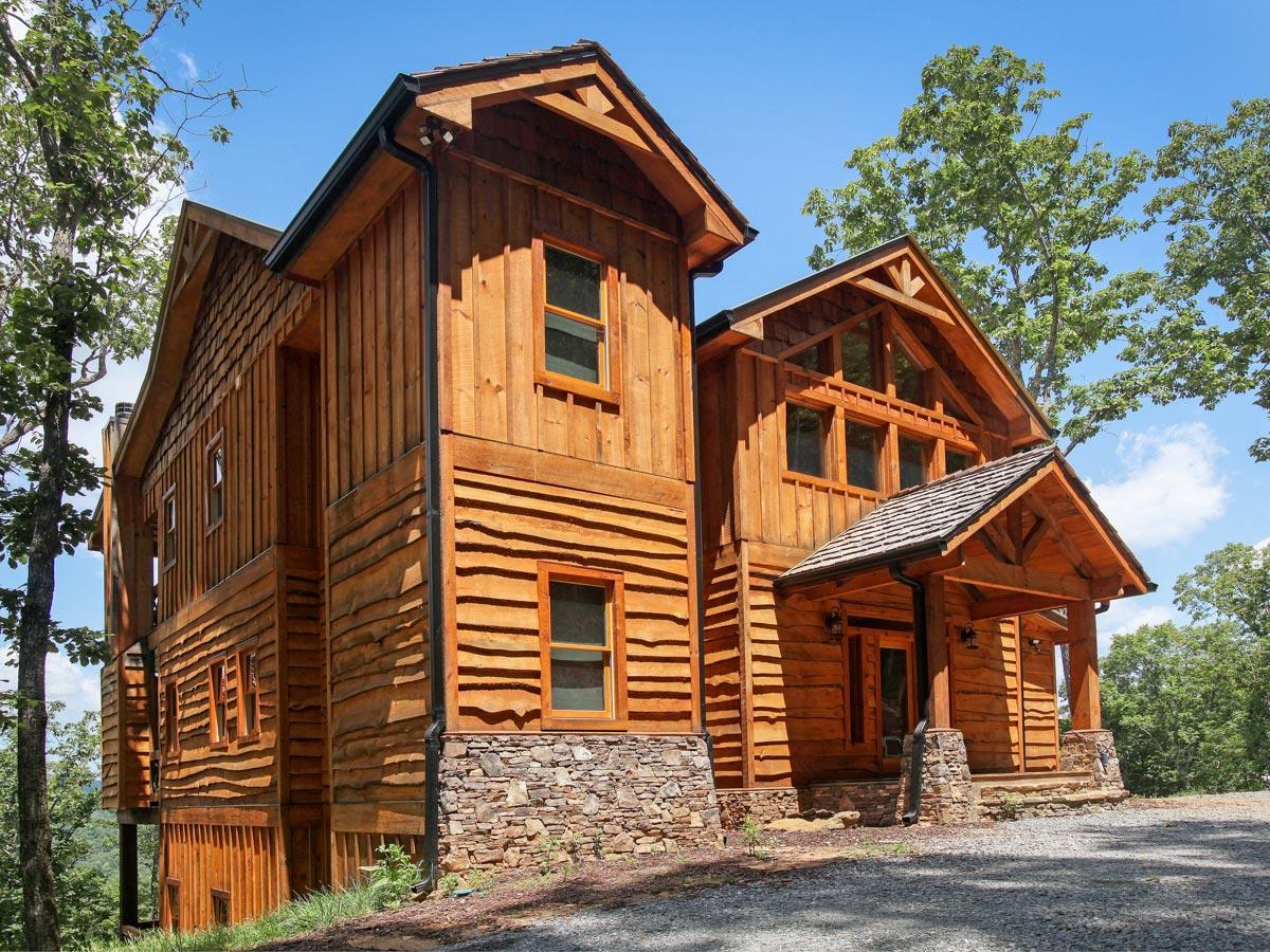 House plan exterior. Two-story rustic style home with a gabled roof, stone foundation, and covered entry porch with timber frame construction.